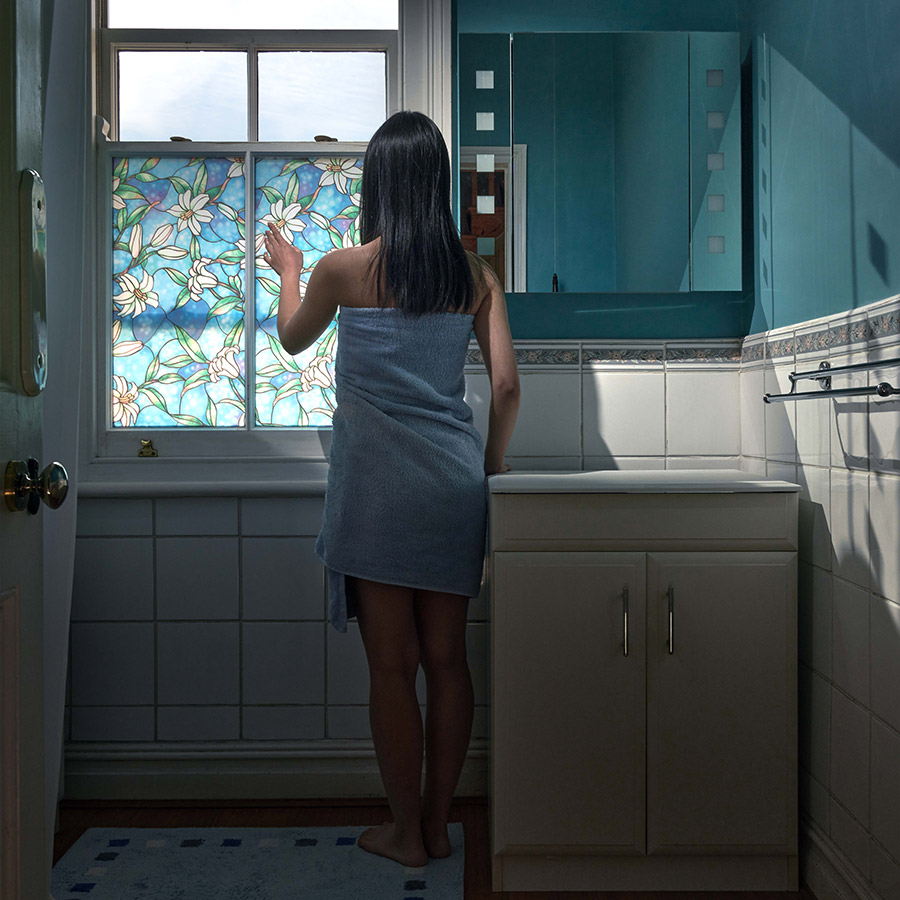girl wrapped in blue towel reaches towards bathroom window