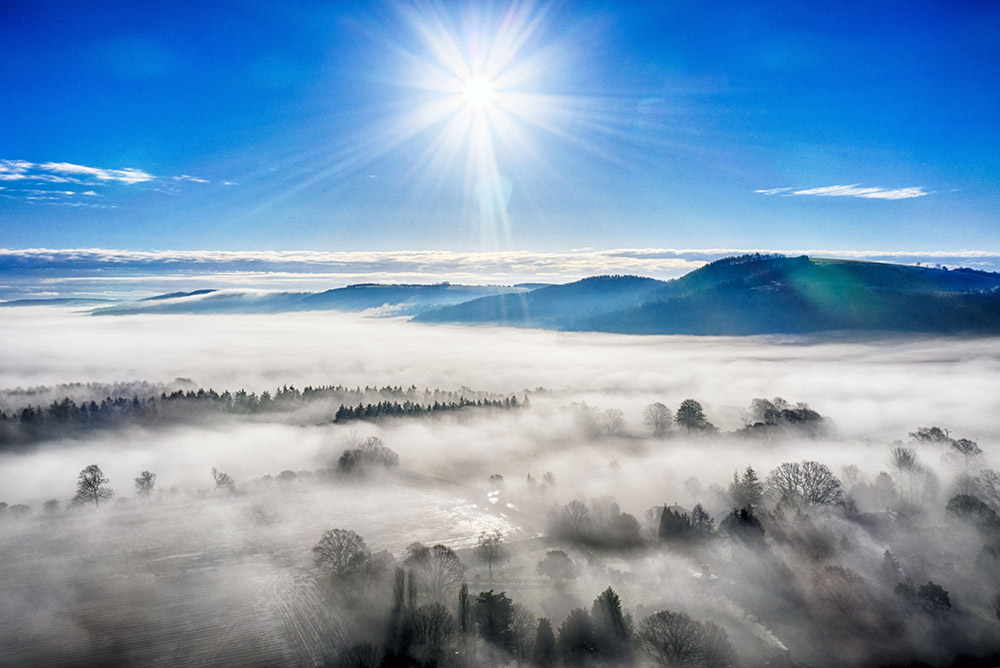 looking over forest and mountain scene bright blue sunny sky and mist over trees