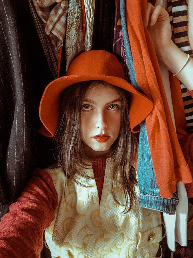 girl in red hat poses amongst hanging clothes