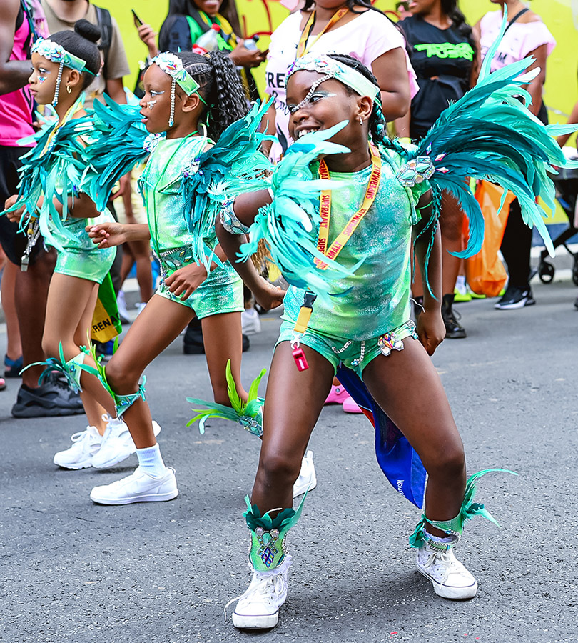 children wearing green outfit and feathers dancing down notting hill carnival