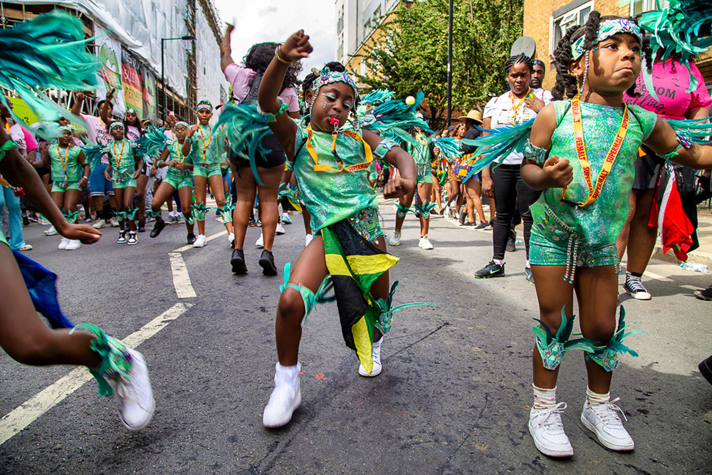 children dancing in feathers down street of notting hill carnival