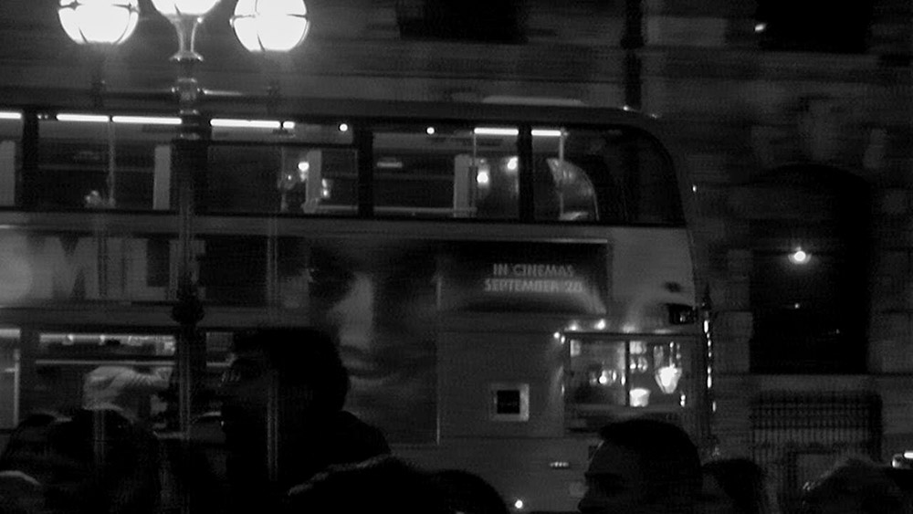 black and white night double decker bus in london with smile horror film poster on