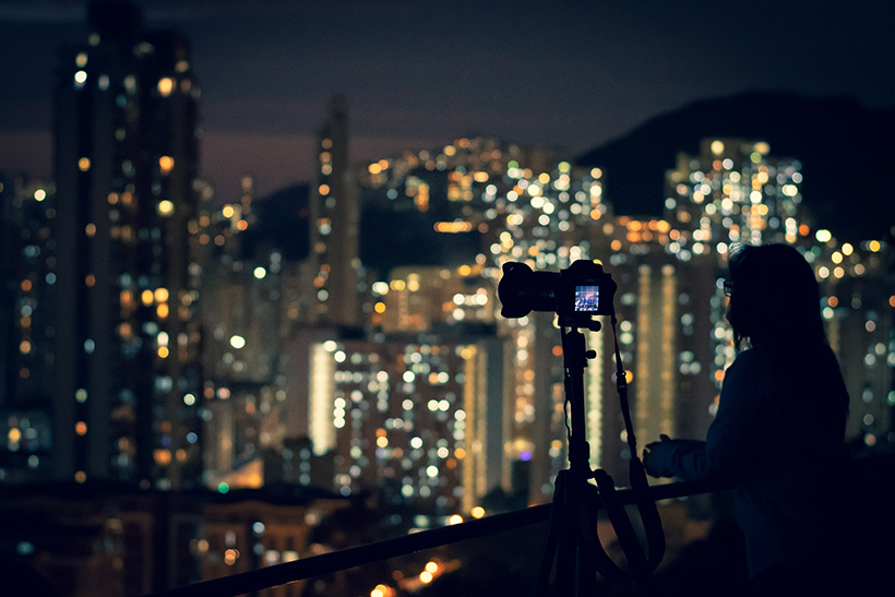 Siluette of a person and camera photographing the Night Cityscape. In the background out of focus lights of a big city.