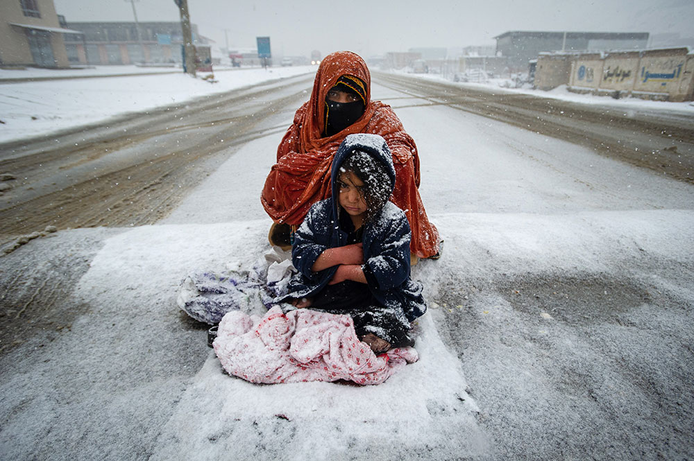 ‘An Afghan woman begs for money from passing cars in the snow, with her child huddled beside her by Scott Peterson/Getty Images