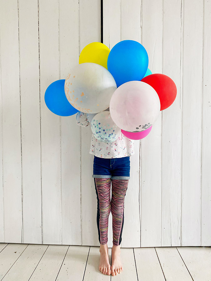 person posing holding a bunch of different coloured balloons in front of face