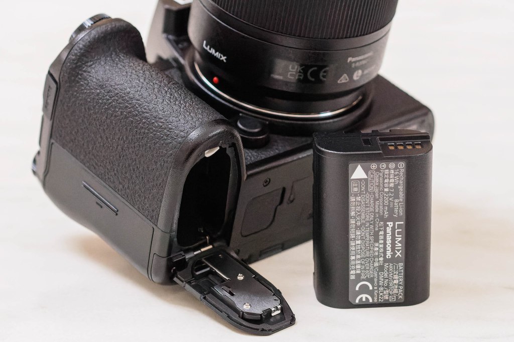 Panasonic Lumix S5II bottom, with battery door open, and a battery placed next to the camera