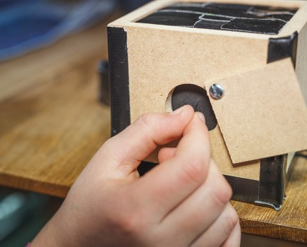 piercing black paper with a pin to make pinhole camera lens