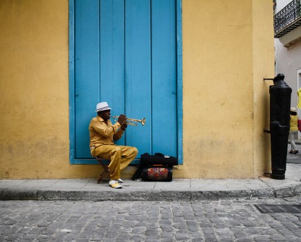 man wearing yellow suit sat in front of blue door playing trumpet in havana