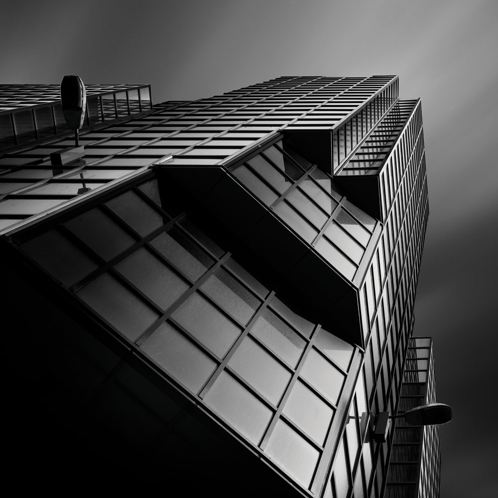 Black and white building photography,Billy Currie. Upwards, tilted perspective of a building with reflective glass surface.