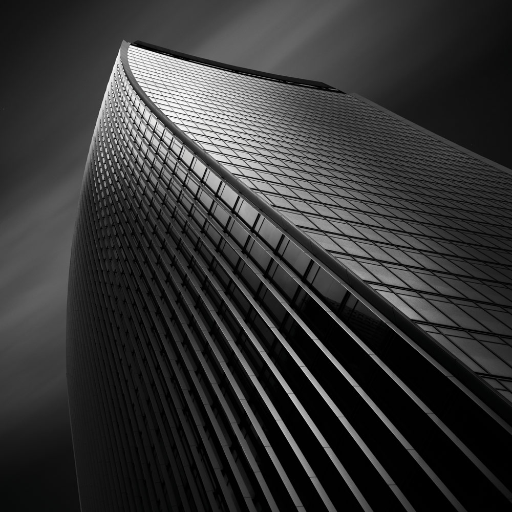 Black and white building photography, Billy Currie. Modern high rise glass surfaced building photographed from below, long exposure, wispy clouds in the background.