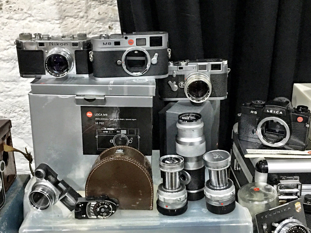 Cameras, including Leica and Nikon cameras, on a table along with some lenses