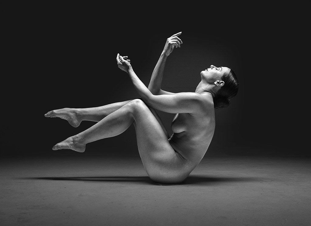 nude woman curled in a pose head and hands pointing up sat n ground