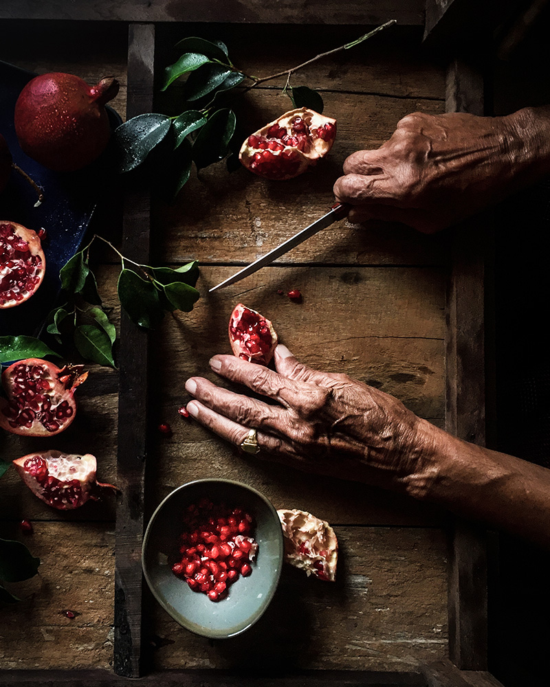 old man hands cutting up pomegranates on a wooden board