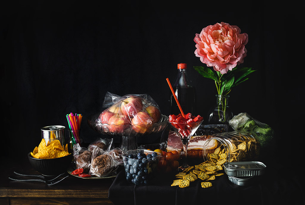 food and flower still life against black background, food contained in plastic