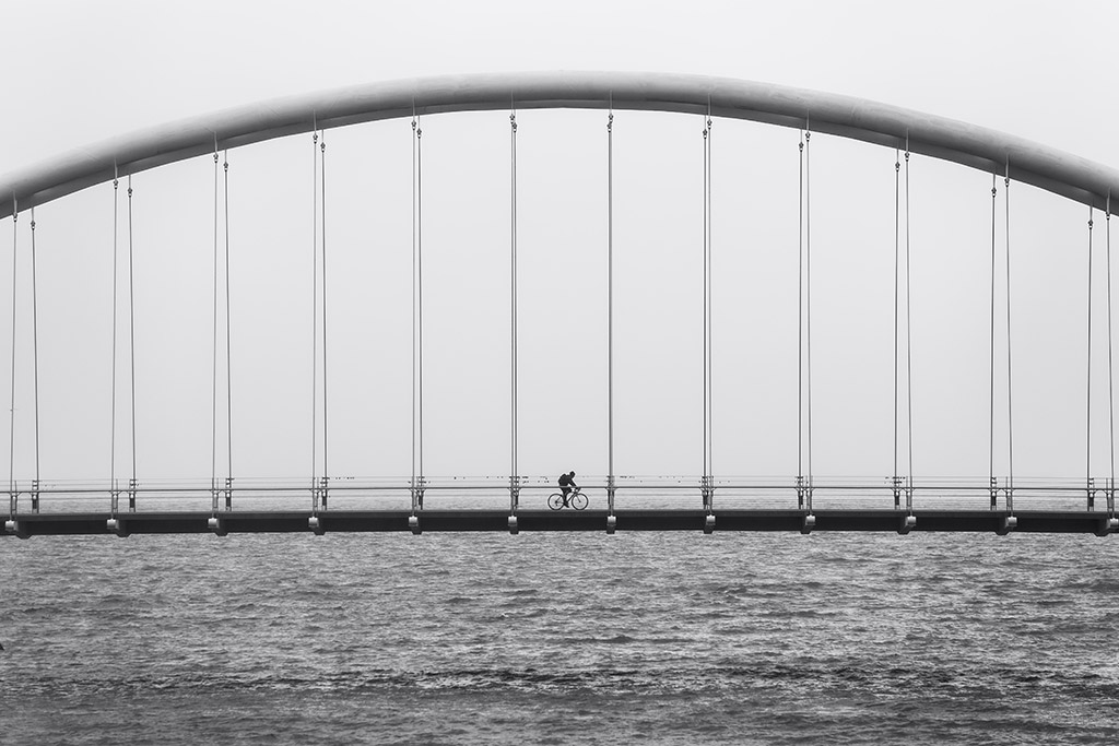 silhouette of a person cycling across bridge alone