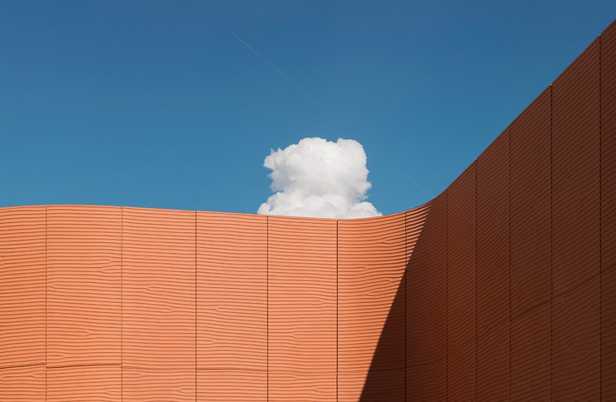 abstract architecture photograph of brick red building against blue sky and single cloud