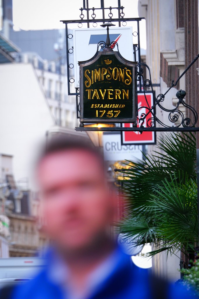 Simpsons Tavern Sign in focus in the background. In the foreground out of focus face of a passerby. Shot on Fujifilm X-H2S