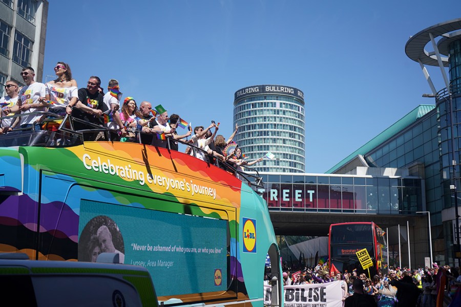 Birmingham pride bus with rainbow looking at crowd and bullring building