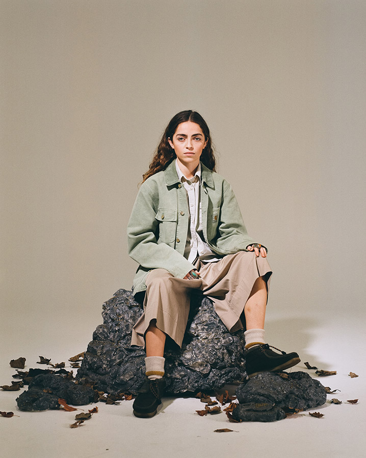 model in green coat sat on a large rock in studio space for portrait