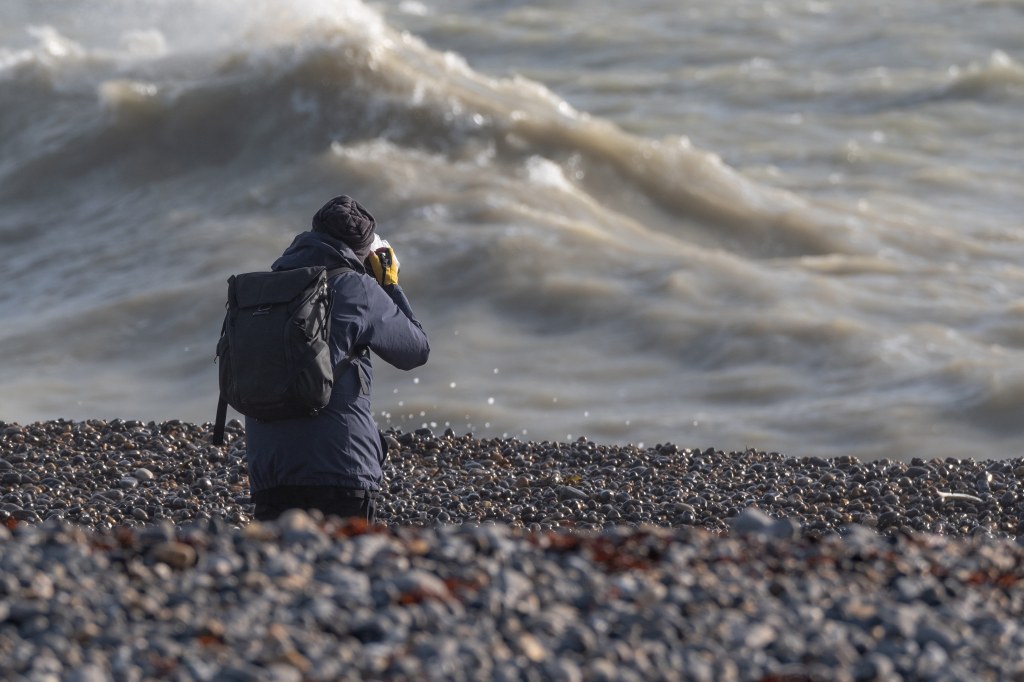 A photographer on a pebbly beach taking photos of the water and waves