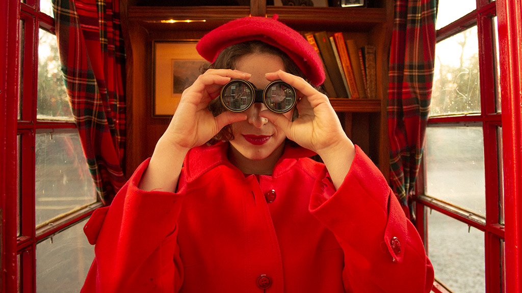 girl in red beret and coat holding binoculars up to face photography graduate