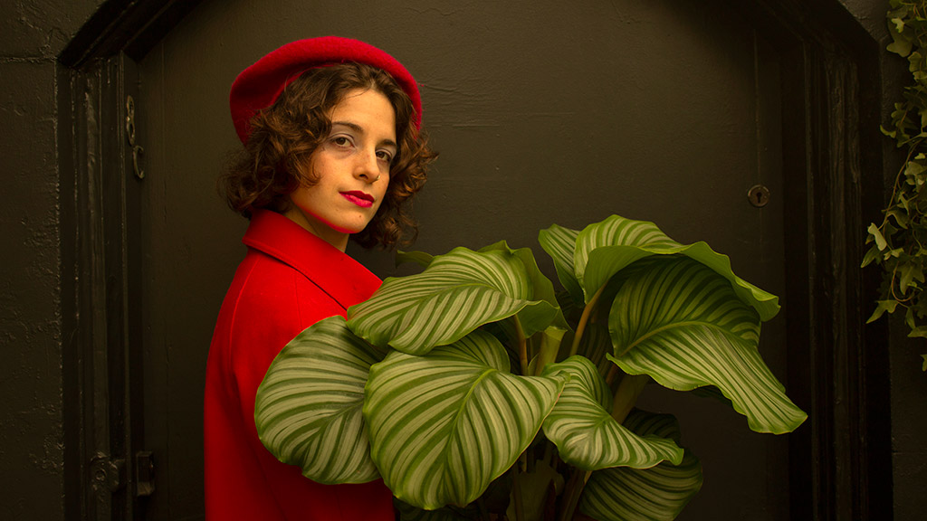 girl in red coat and beret holding a house plant in style of wes anderson