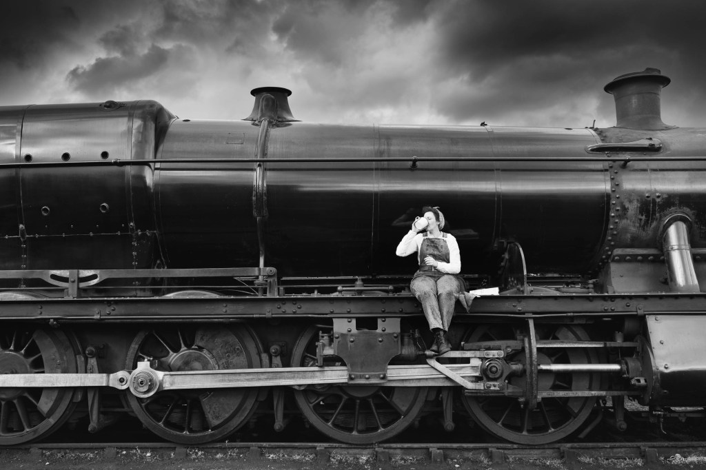 Woman drinking from a tea cup sitting on the side of a steam train. Nik Collection 6 Silver Efex test.