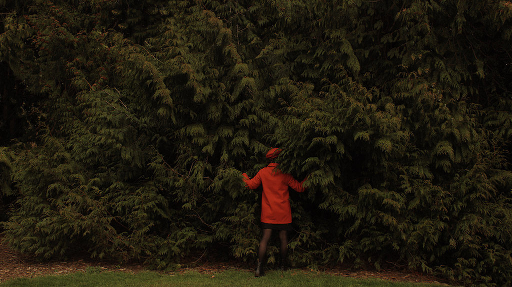 girl in red coat and beret walking into fir trees