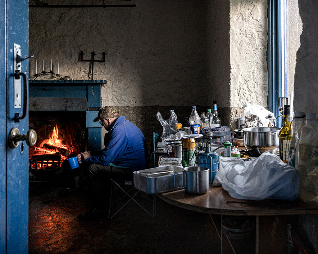 man making a fire inside the bothy surrounded by empty cans and food wrappers