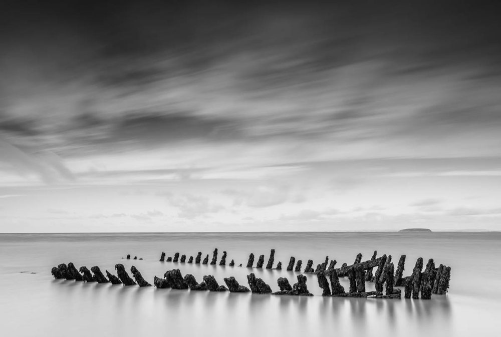 Lightroom's black and white interface, edited final image in black and white of an old wooden shipwreck sticking out from the sand in Nornen beach near Burnham-on-Sea in Somerset. 
