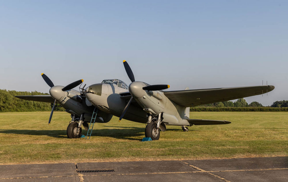 Lightroom vs Photoshop, using layers, an old grey two propeller military plane on the ground against a blue cloudless sky