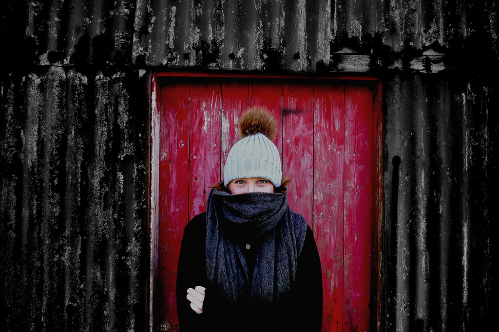 person stood infront of wooden red door in woolly hat and thick scarf