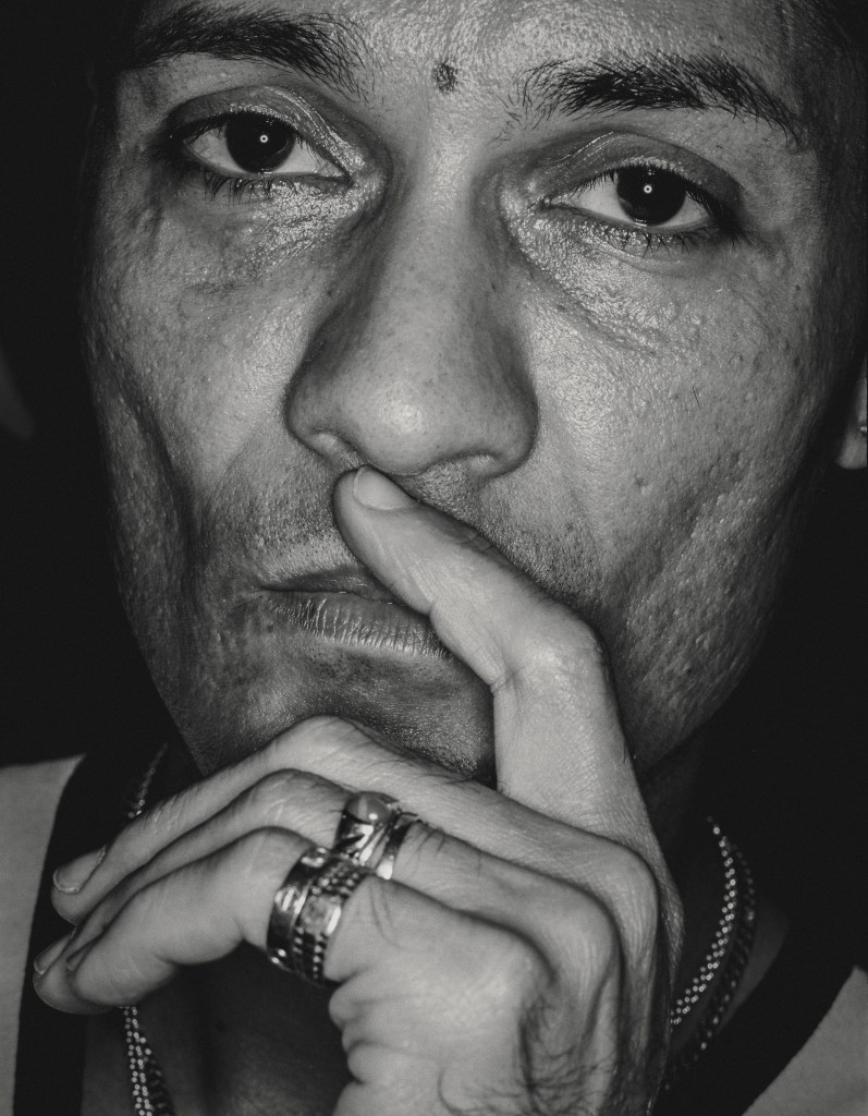 Close up black and white analogue portrait shot of a man his hand in front of his mouth one finger touching his upper lip, in a thinking pose. 
