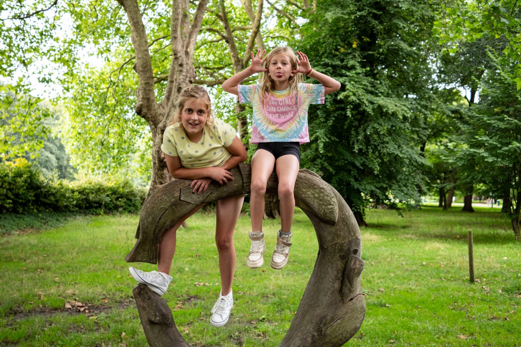 Nikon Nikkor 24mm f/1.7 lens sample image portrait of two kids sitting and climbing to a wooden sculpture, making faces.