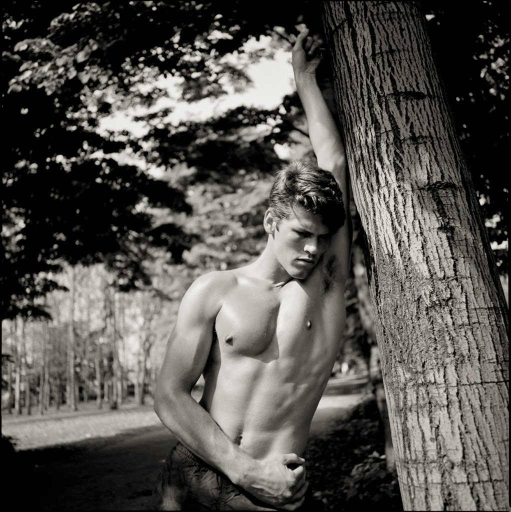 A young man in trousers leaning against a tree, Black and white,