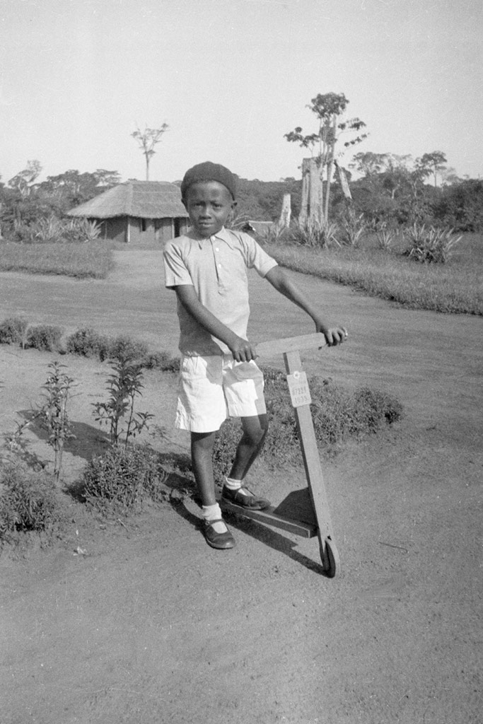 Young Black boy on a wooden scooter, in a rural setting.