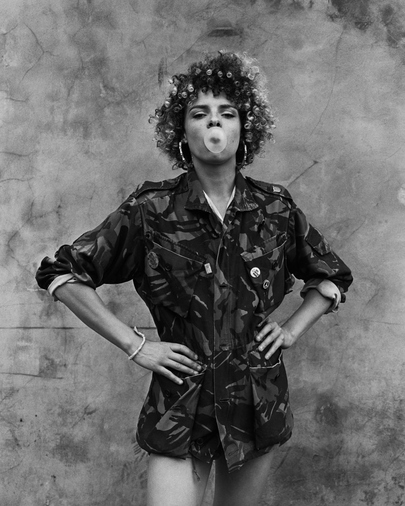 simon murphy, black and white analogue portrait of a woman blowing a bubblegum, her hands on her waist. Power pose, facing the camera.