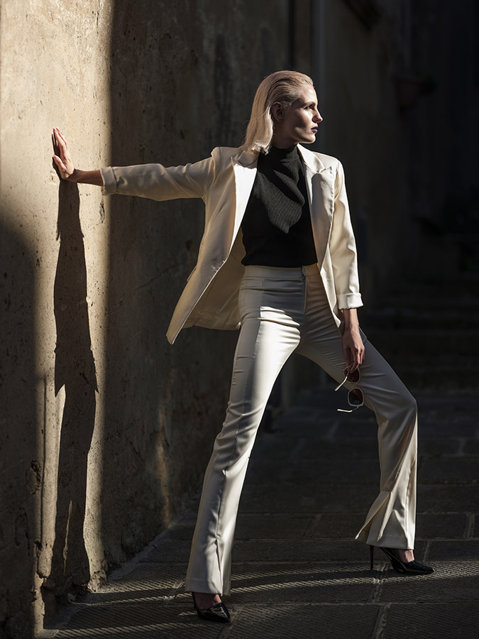 model in white suit posing in hard light posing against wall