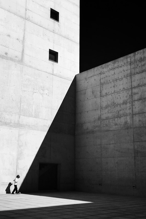 minimalist architecture in harsh strong summer light with child playing with a ball towards shadow