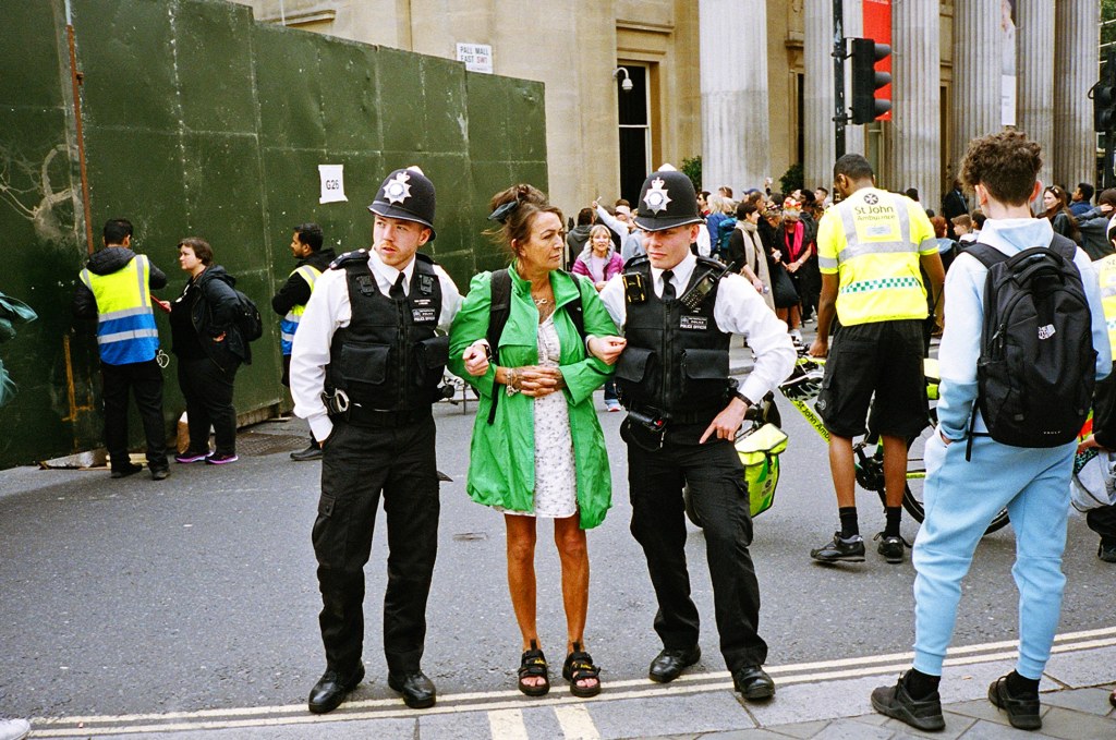 Two policemen locks arms with a woman to restrain her in what appears to be a protest.