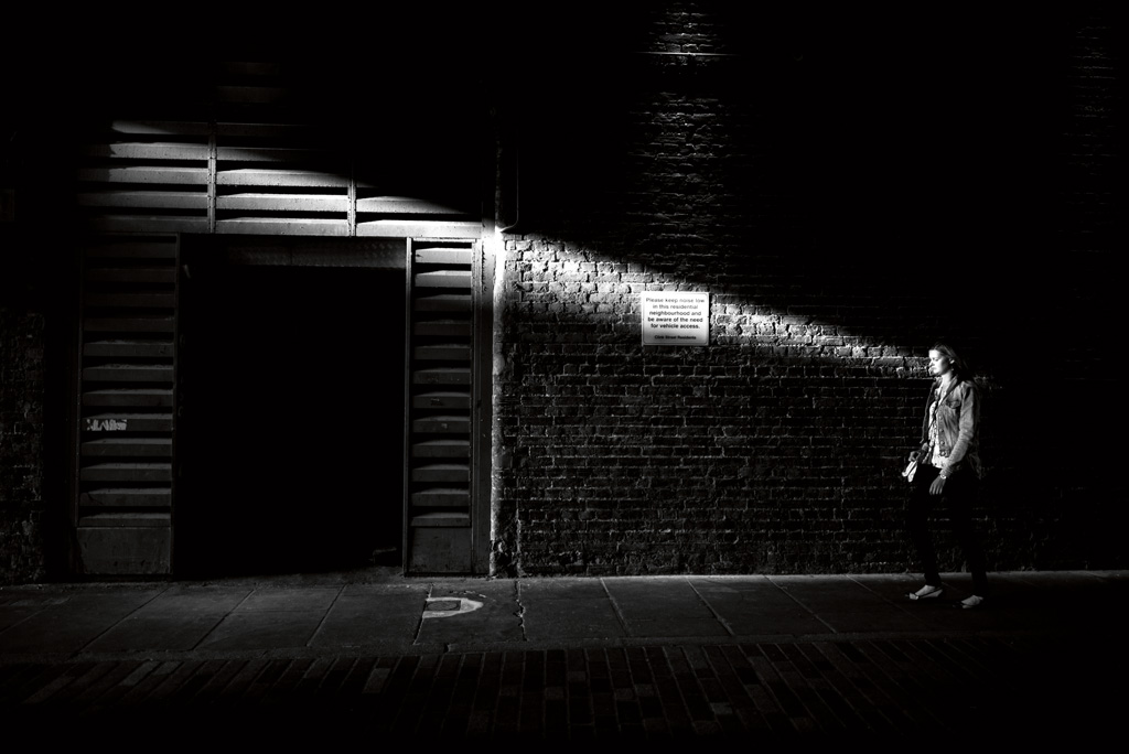a narrow light streak in an alleyway illuminates a woman walking