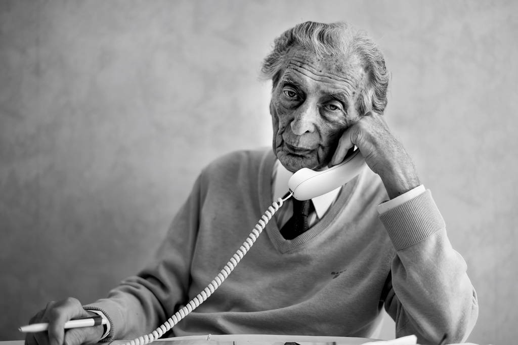 older man sat at a desk on telephone