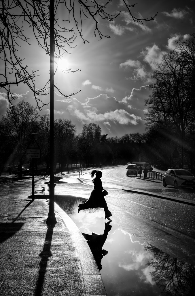 woman jumping over a puddle next to road curb