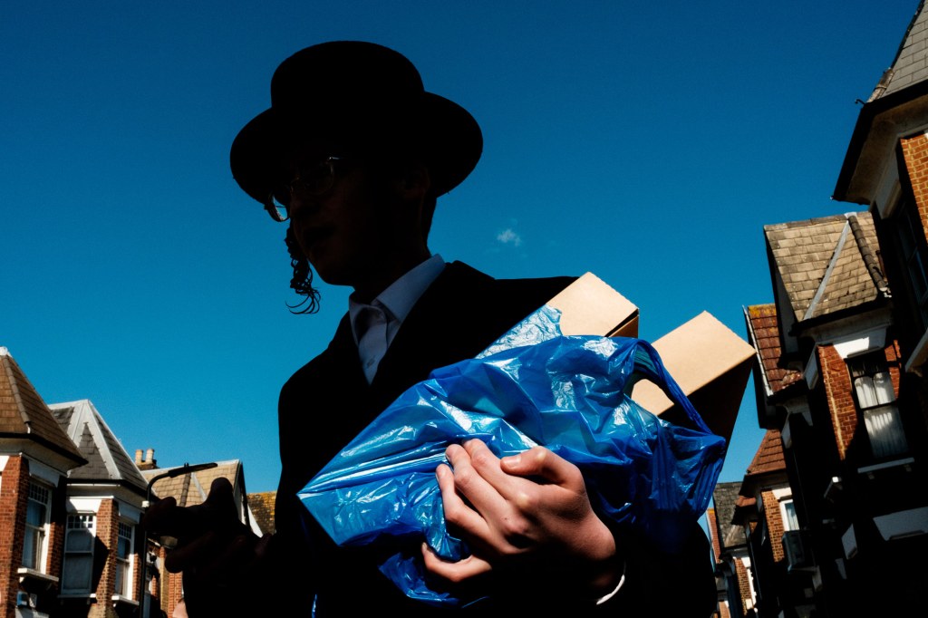 Jewish man carrying two packages in a blue carrier bag photographed from below, his face is obscured by shadows.