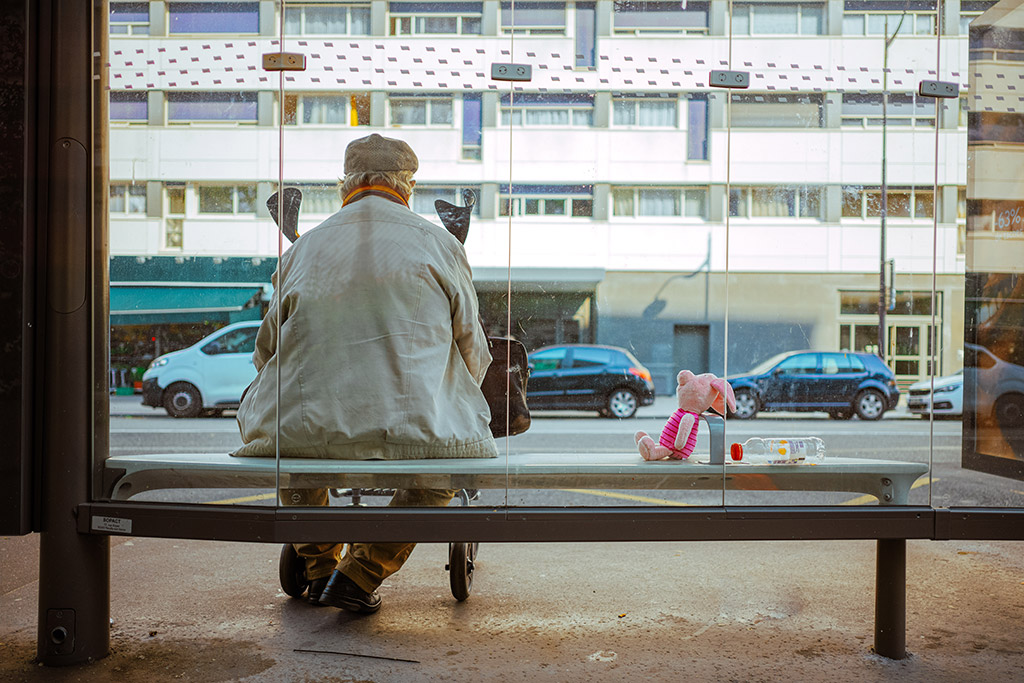 elderly man sat at a bus stop with a piglet plushie sat next to him