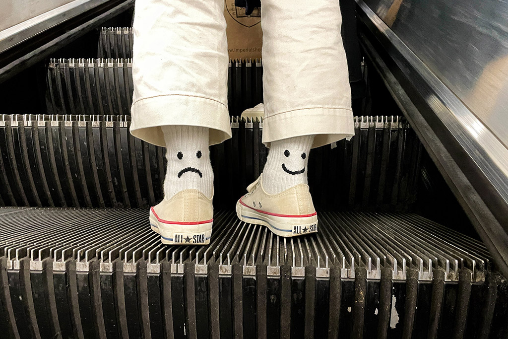 persons feet on escalator with socks showing smiling face on one ankle, sad face on other
