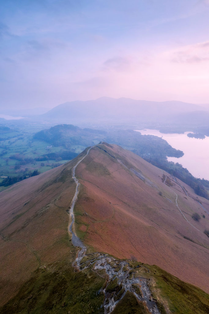 Aerial photography-Mountain ridge with a path leading right on its crest, purple hazy sunset in the background