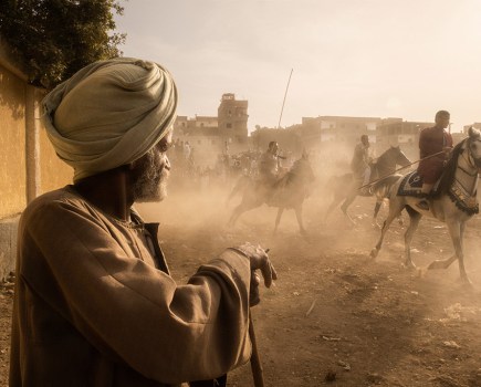 street portrait of a man looking at dust being kicked up by the horses’ hooves