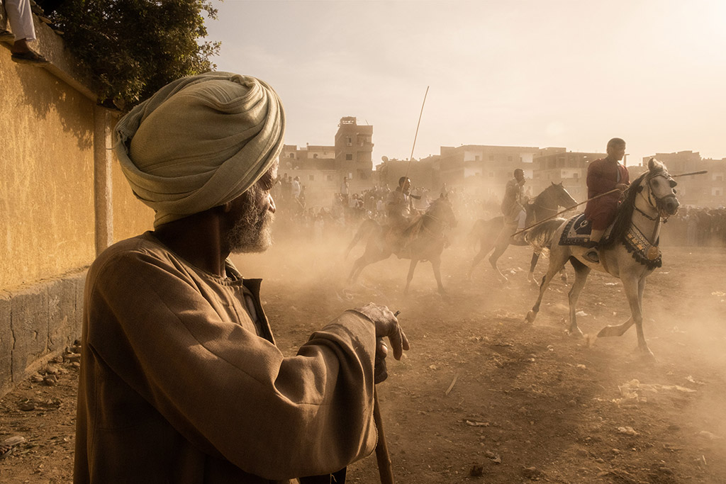 street portrait of a man looking at dust being kicked up by the horses’ hooves