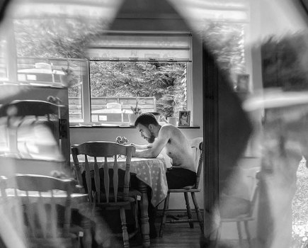 person sat at a kitchen table looking through glass iphone 12